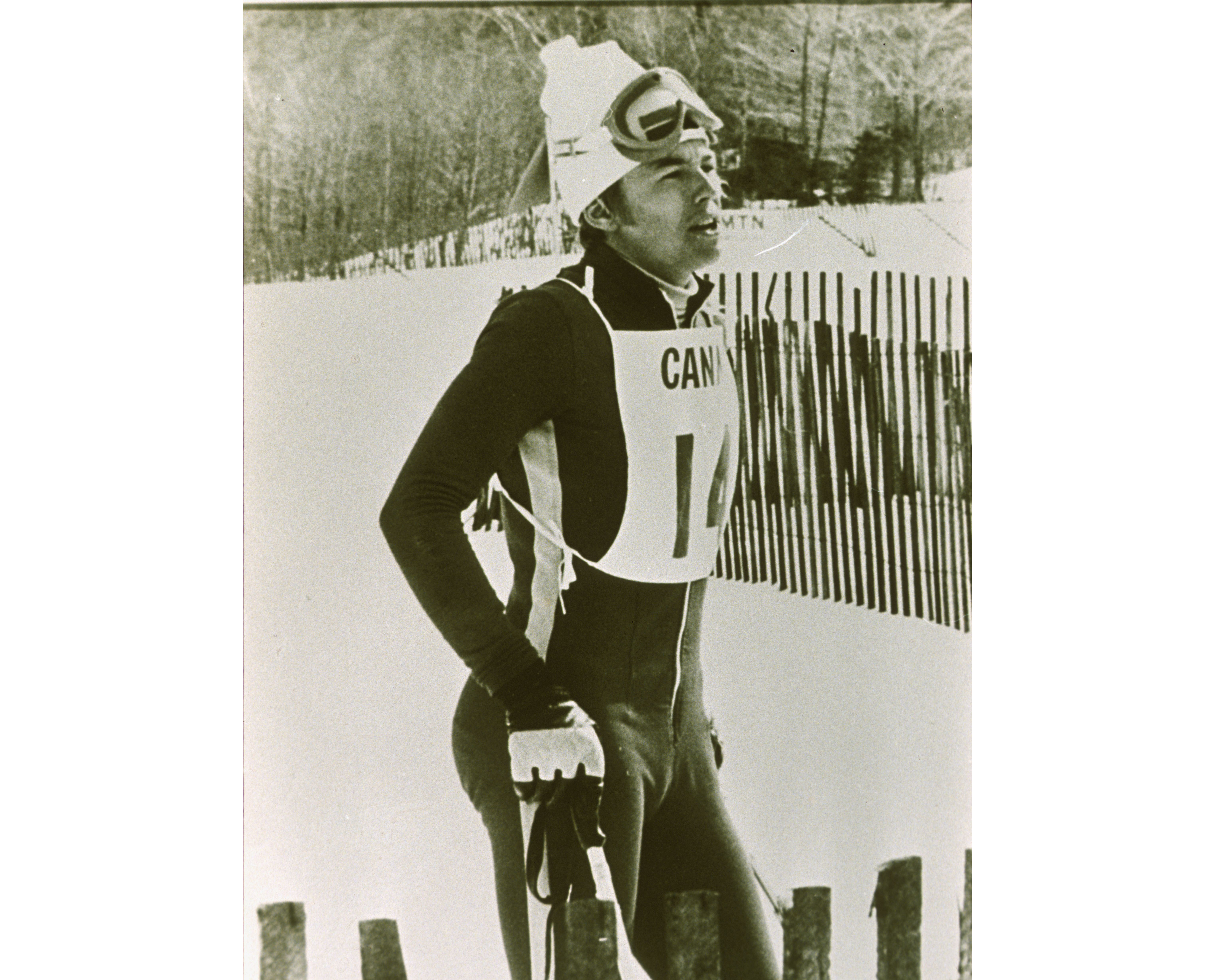 On a mountainside, Otto stands with ski poles and a racing suit. 