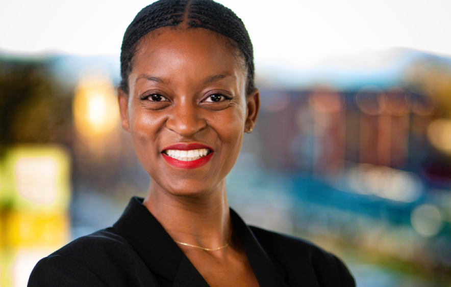 A headshot of a smiliing black woman with the University of Denver behind her.